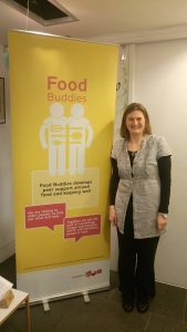 A woman smiling in front of a Food Buddies banner