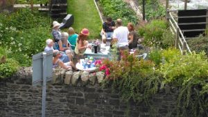 Group of people around 2 tables in a sunny community garden.