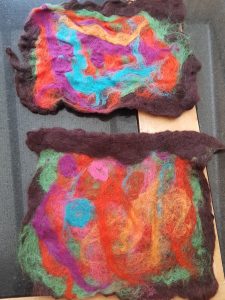 Photo of 2 finished felt artworks, with abstract green, red, orange, purple and blue wool on a black background